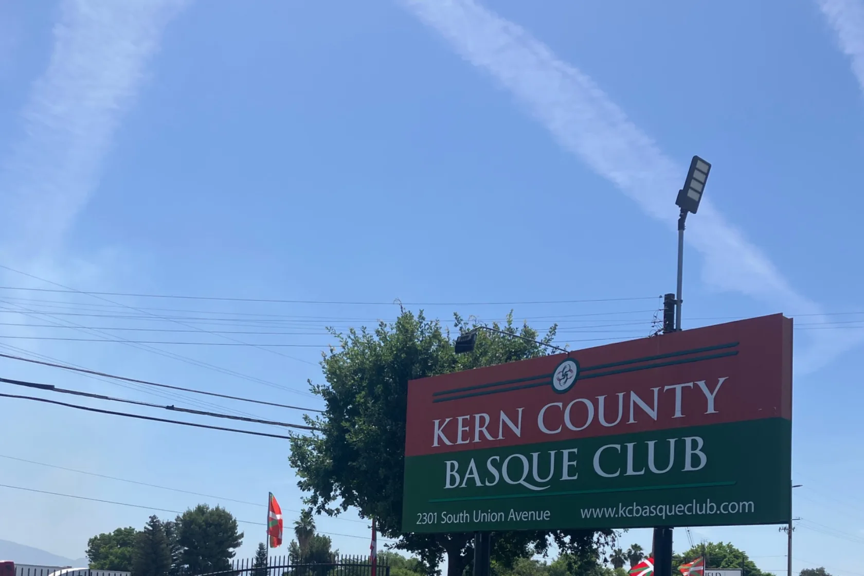 The red and green roadside sign of the Kern County Basque Club standing against a bright sky